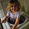 child, washing_machine, curly_hair, laundry_room, playful, smiling, indoor, appliance, white, clothing, person, young, cute, curly, funny, home, exploring, childhood, happy, adventure