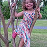 child, tree, smiling, outdoor, grass, dress, pink_shoes, curly_hair, nature, park, branches, happy, person, playful, summer, casual_clothing, young, leisure, greenery, daylight