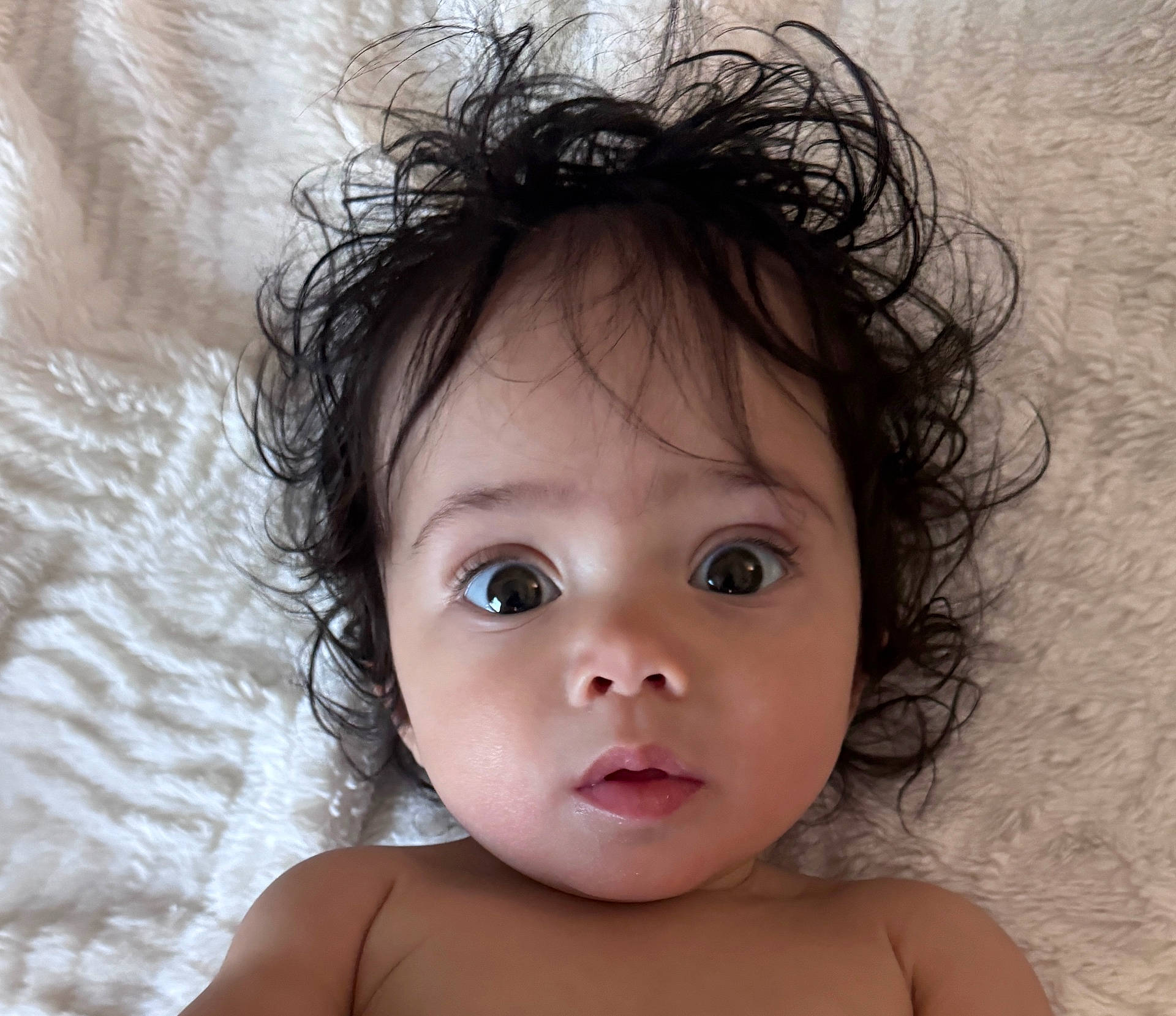 Willow is registered to the contest to win money with this photo: baby, blanket, child, closeup, curly_hair, cute, expression, eyes, face, hair, indoors, infant, lying_down, mouth, nose, person, portrait, skin, texture, young_child