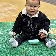 Mathéo participe au concours pour gagner de l'argent avec cette photo : toddler, child, smiling, jacket, chalk, playground, outdoor, sitting, sock, happy, face, person, toy, ground, colorful, casual_clothing, cute, young_child, play, daytime