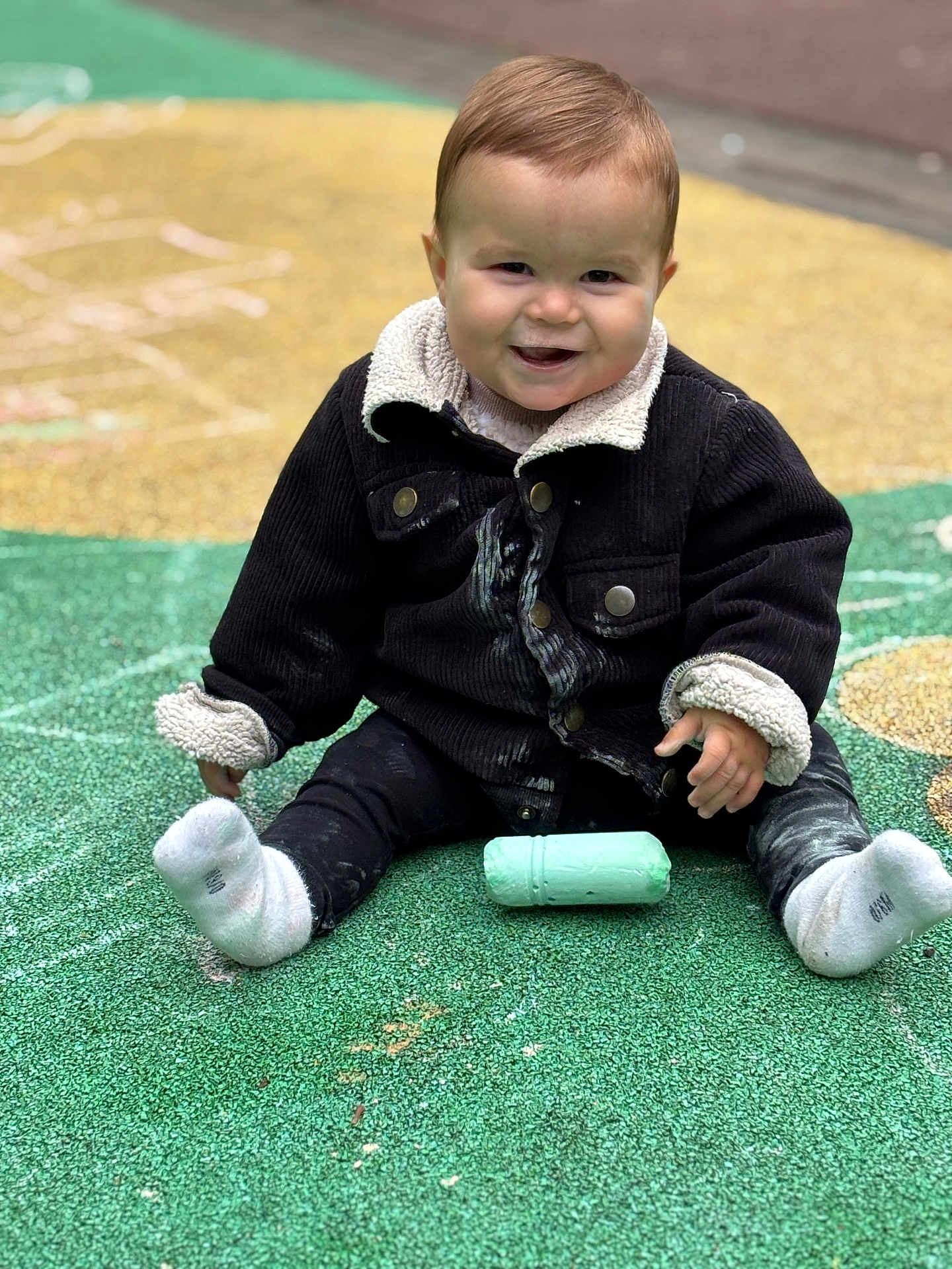 Mathéo participe au concours pour gagner de l'argent avec cette photo : toddler, child, smiling, jacket, chalk, playground, outdoor, sitting, sock, happy, face, person, toy, ground, colorful, casual_clothing, cute, young_child, play, daytime