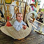 toddler, child, carousel, swan, ride, amusement_park, outdoor, wooden_floor, decorative, playful, daylight, cute, portrait, seat, toy, fun, person, expression, clothing, baby