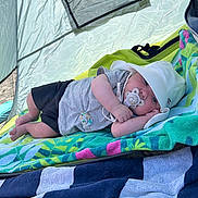 Nolan a rejoint le concours — aidez-le/la à gagner de superbes lots ! baby, baby_boy, blanket, child, clothing, colorful, cute, hat, infant, lying_down, outdoor, pacifier, relaxing, resting, shade, soft_light, summer, sun_hat, tent, towel