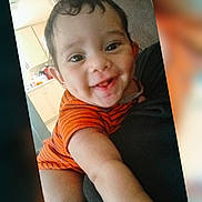 Levi is registered to the contest to win money with this photo: baby, child, smiling, orange_clothing, striped_clothing, face, arm, indoor, couch, kitchen, happy, person, infant, young_child, home, furniture, dim_light, cute, portrait, reaching