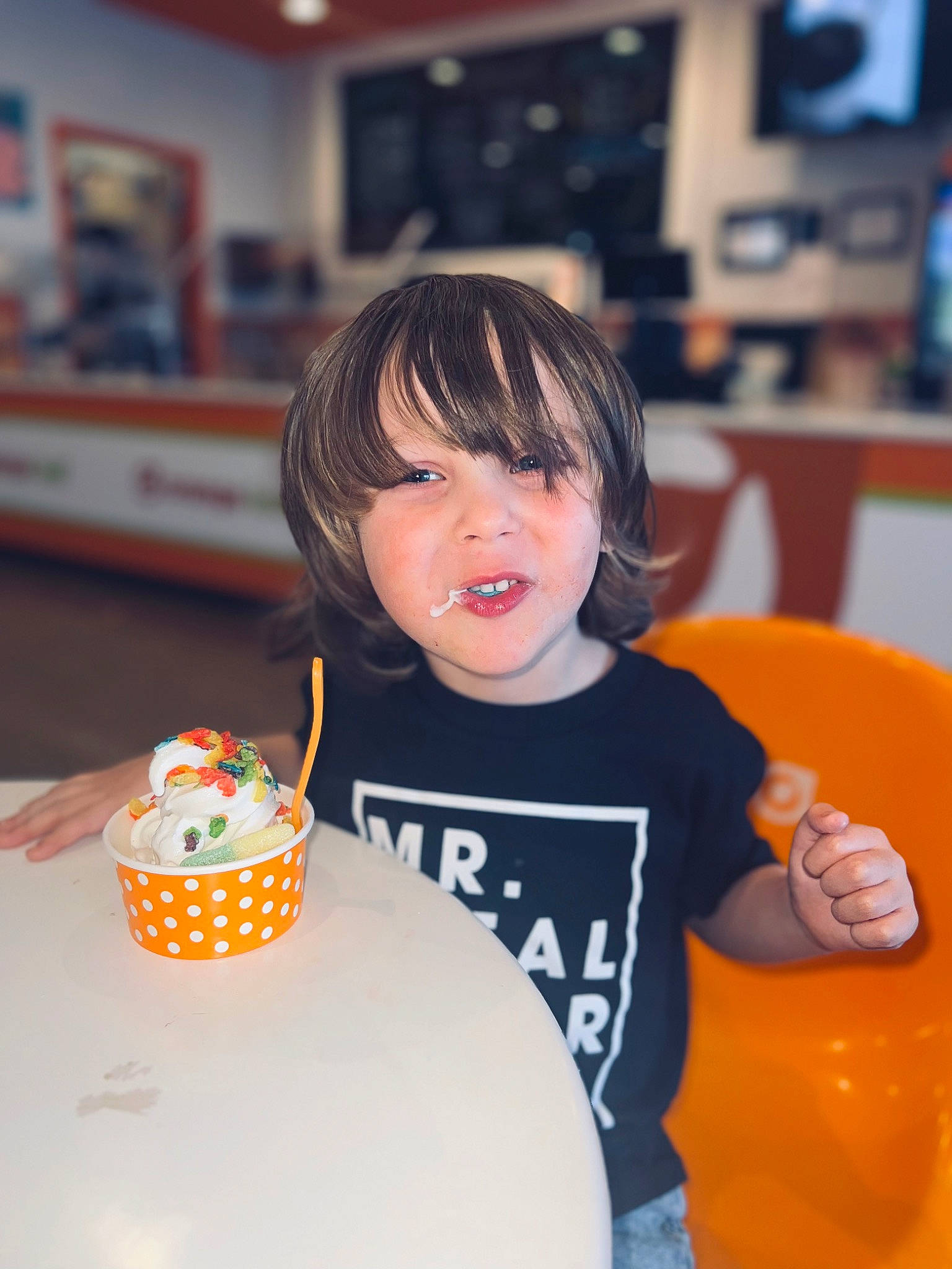 Jalen is registered to the contest to win money with this photo: birthday, chair, child, cup, drink, drinkware, fun, happy, icing, leisure, orange, party, party_supply, person, room, sweetness, t_shirt, table, tableware, television