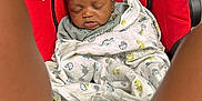 Derreck Jr is registered to the contest to win money with this photo: baby, sleeping, blanket, car_seat, infant, child, red, black, wood_floor, cozy, wrapped, peaceful, indoors, person, legs, pattern, cute, comfort, resting, soft