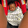 baby, sleeping, blanket, car_seat, infant, child, red, black, wood_floor, cozy, wrapped, peaceful, indoors, person, legs, pattern, cute, comfort, resting, soft