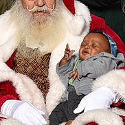 Derreck Jr is registered to the contest to win money with this photo: baby, santa_claus, holiday, christmas, beard, red_hat, white_gloves, smiling, child, festive, red_suit, indoor, portrait, happy, seated, green_background, headband, casual_clothing, white_socks, joyful
