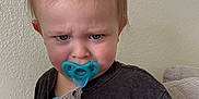 Rylo is registered to the contest to win money with this photo: toddler, child, pacifier, grumpy, rolling_stones, tshirt, indoor, couch, blond_hair, blue_eyes, expression, person, seated, red_blanket, casual_clothing, home, young_child, face, portrait, baby