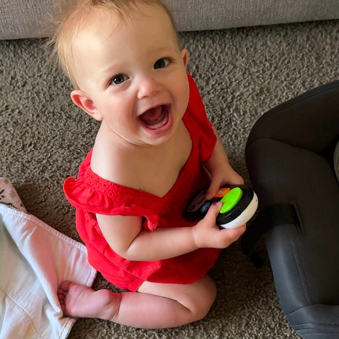Rilynn is registered to the contest to win money with this photo: baby, carpet, cheerful, child, cute, expression, face, hair, happy, holding, indoor, infant, person, play, red_dress, sitting, small, smiling, toddler, toy
