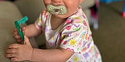 Rilynn is registered to the contest to win money with this photo: baby, pacifier, standing, holding, toy, colorful_clothing, indoor, carpet, couch, child, infant, cute, face, hand, smile, shorts, person, teething_toy, bright, happy