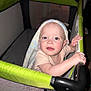 Rilynn joined the competition — help win amazing prizes! baby, child, playpen, towel, indoor, person, holding, grip, face, expression, curious, pink_clothing, blanket, head_covering, light_skin, blue_eyes, infant, standing, mesh_sides, home