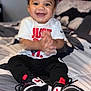 Jamir joined the competition — help win amazing prizes! child, toddler, smiling, clapping, sitting, bed, sneakers, white_tshirt, black_pants, indoor, happy, curly_hair, casual_clothing, footwear, person, portrait, young_child, cute, joyful, clothing