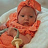 baby, infant, orange_outfit, headband, pacifier, blanket, soft_texture, lying_down, cute, child, newborn, comfort, portrait, indoors, person, apparel, sleepwear, resting, young_child, cozy