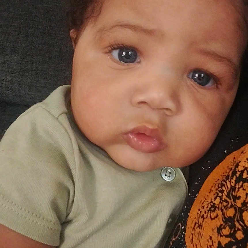 Mikouri Hill is registered to the contest to win money with this photo: baby, button, casual, child, close_up, clothing, couch, curly_hair, cute, expression, eyelashes, face, family, indoor, person, portrait, skin, soft_light, toddler, young_child