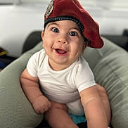 Marius participe au concours pour gagner de l'argent avec cette photo : baby, beret, red_hat, smiling, happy, infant, white_onesie, cushion, indoor, person, cute, chubby_arms, face, portrait, soft_lighting, closeup, sitting, reaching, expression, young_child