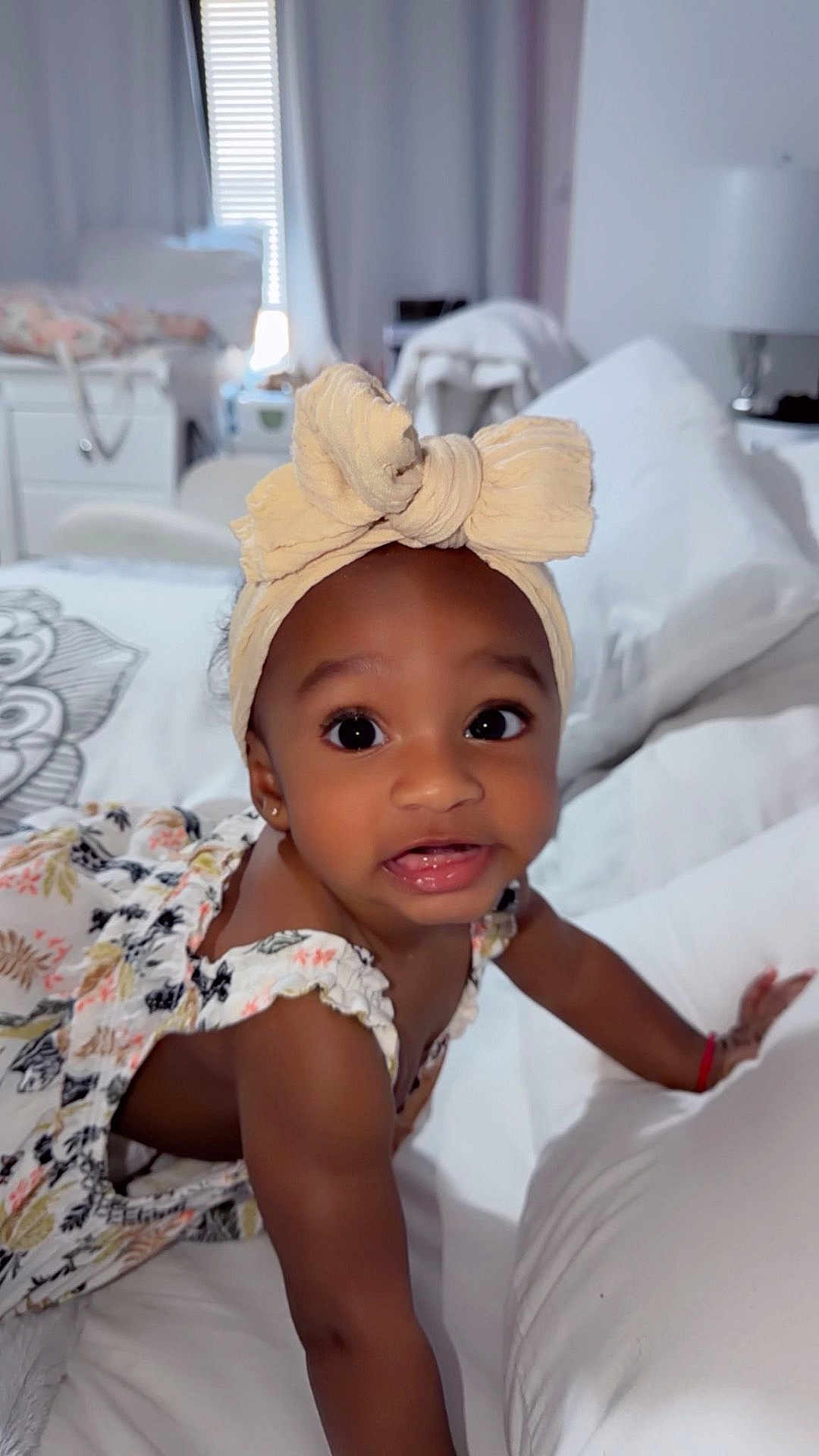 Aisha joined the competition — help win amazing prizes! baby, child, headband, bow, crawling, bed, pillow, white, curious, indoors, smiling, clothing, person, infant, cute, expression, soft_lighting, home, face, young