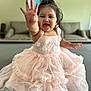 toddler, child, smiling, pink_dress, indoor, happy, reaching_hand, sitting, face, person, cute, portrait, furniture, couch, home, wall_art, soft_lighting, baby, young_child, playful