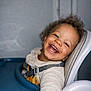 Fabio a rejoint le concours — aidez-le/la à gagner de superbes lots ! child, toddler, smiling, laughing, curly_hair, high_chair, tray, harness, bib, teeth, eyes, face, portrait, indoor, cozy_clothing, hand, cheerful, candid, seat, background_wall