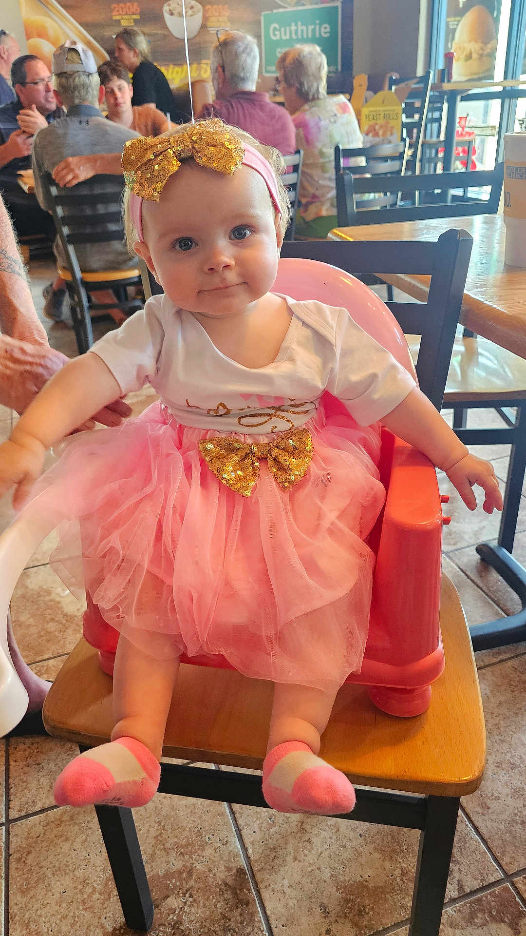 Dawn joined the competition — help win amazing prizes! baby, child, tutu, pink, golden_bow, headband, high_chair, restaurant, table, chair, floor_tile, socks, person, indoor, cute, smiling, seated, people, background, casual