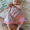 baby, casual_clothing, child, curious_expression, cute, fish_applique, floral_pattern, foot, hand_in_mouth, indoors, infant, leg, lying_down, pacifier, person, pink_dress, relaxed, skin, soft_blanket, tattoo