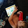 child, tablet, red_cup, blanket, couch, indoors, relaxing, device, screen, learning, hand, young_child, casual, comfort, technology, drinking, skin, resting, home, portrait