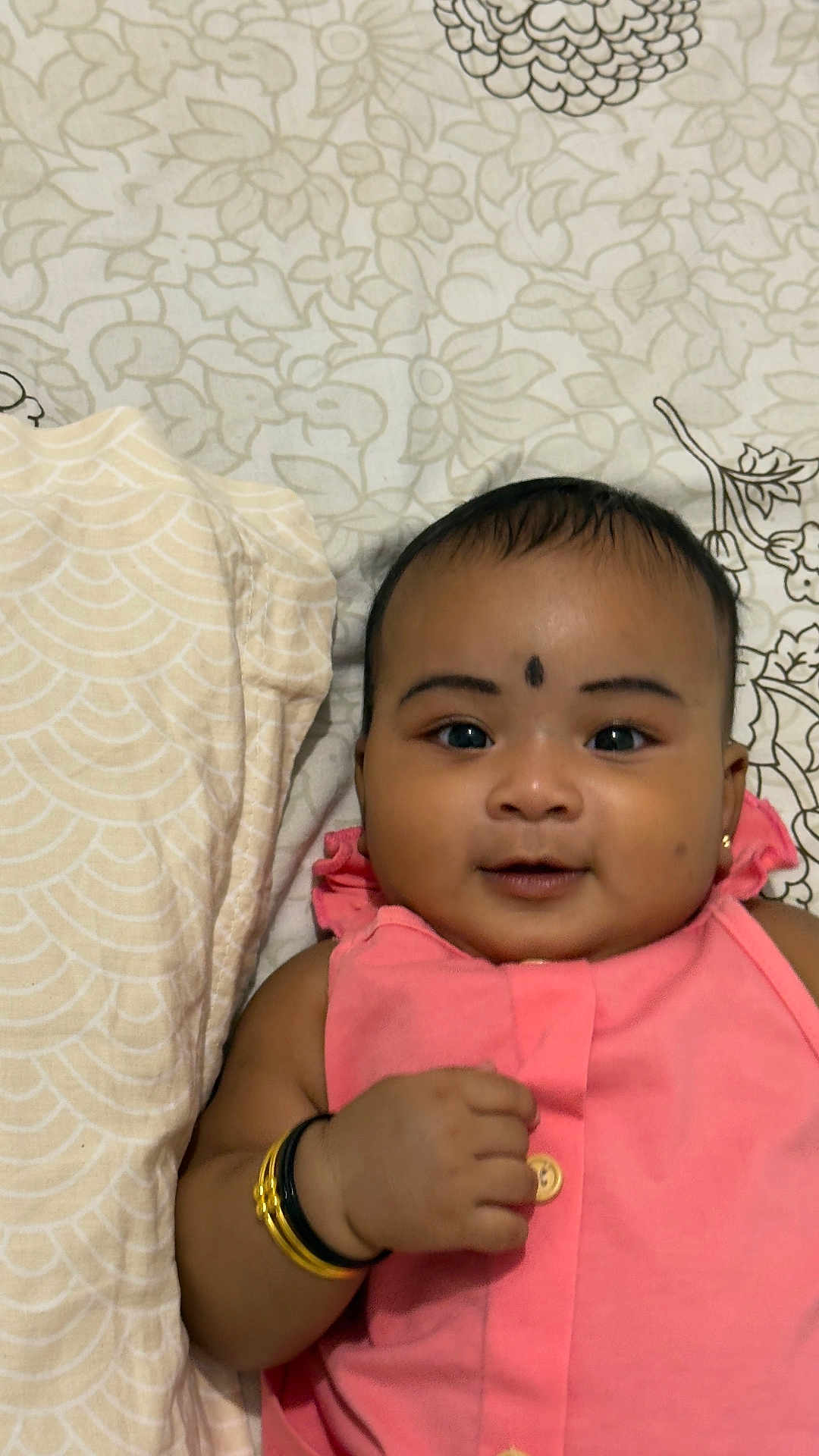 Ekaksha joined the competition — help win amazing prizes! baby, infant, smiling, pink_clothing, bracelet, face, lying_down, bedspread, patterned_background, cute, child, adorable, portrait, indoors, young_child, happy, closeup, skin, hand, person