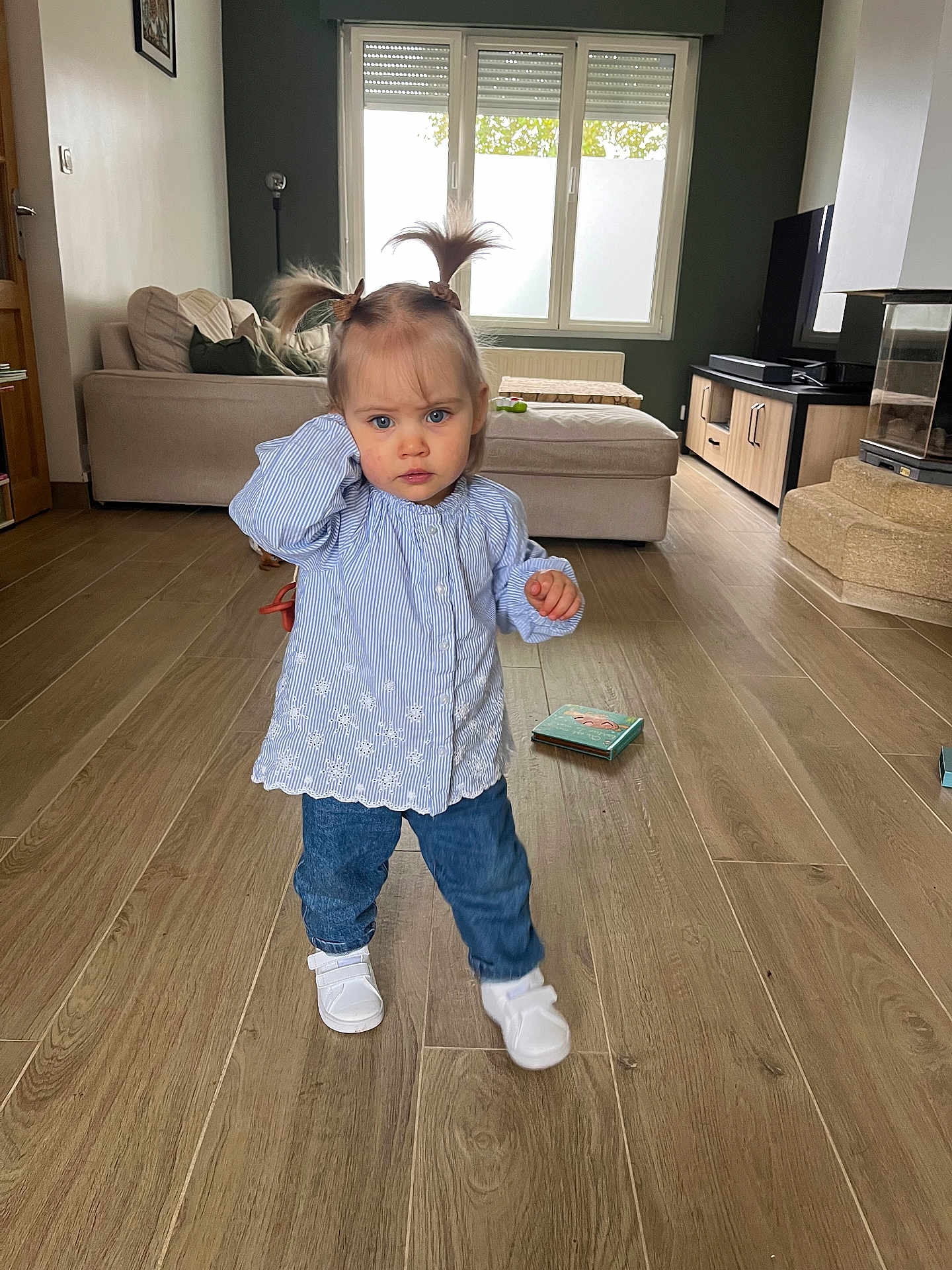 Alice a rejoint le concours — aidez-le/la à gagner de superbes lots ! blue_blouse, book, casual_clothing, child, curtains, cushion, fireplace, flooring, home, indoor, jeans, living_room, person, pigtails, sofa, television, toddler, white_shoes, window, wooden_floor