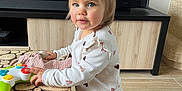 Alice participe au concours pour gagner de l'argent avec cette photo : toddler, child, toy, controller, pajamas, heart_pattern, wooden_table, living_room, floor, blue_eyes, blond_hair, slippers, furniture, curious, standing, indoor, person, cute, play, home