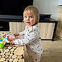 toddler, child, toy, controller, pajamas, heart_pattern, wooden_table, living_room, floor, blue_eyes, blond_hair, slippers, furniture, curious, standing, indoor, person, cute, play, home