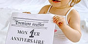 Juliette participe au concours pour gagner de l'argent avec cette photo : baby, blue_eyes, celebration, child, clothing, cute, first_birthday, hair_tie, happy, holding, indoor, light, newspaper, portrait, sign, sitting, skin, smiling, toddler, white_background