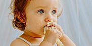 Juliette a rejoint le concours — aidez-le/la à gagner de superbes lots ! toddler, child, blue_eyes, cake, messy, food, eating, cute, portrait, indoors, soft_lighting, white_background, tank_top, hair_tie, close_up, baby, hand, face, curious, sitting