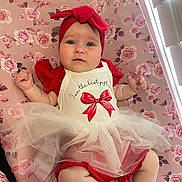 Gracie is registered to the contest to win money with this photo: baby, infant, child, headband, bow, dress, red_clothing, tulle_skirt, blanket, floral_pattern, pink, lying_down, indoors, cute, chubby_cheeks, blue_eyes, curious_expression, soft_lighting, portrait, person