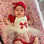 baby, infant, child, headband, bow, dress, red_clothing, tulle_skirt, blanket, floral_pattern, pink, lying_down, indoors, cute, chubby_cheeks, blue_eyes, curious_expression, soft_lighting, portrait, person