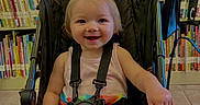 Koura joined the competition — help win amazing prizes! toddler, stroller, child, smiling, rainbow_skirt, indoors, bookshelf, books, happy, baby, seatbelt, floor, library, person, colorful, clothing, cute, portrait, sitting, young_child
