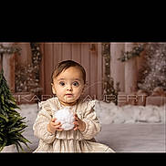 Yara a rejoint le concours — aidez-le/la à gagner de superbes lots ! baby, child, christmas_tree, cozy, curious, cute, decorations, dress, festive, holding, holiday, indoor, portrait, seated, smiling, soft_lighting, toddler, white_ball, winter, young_child