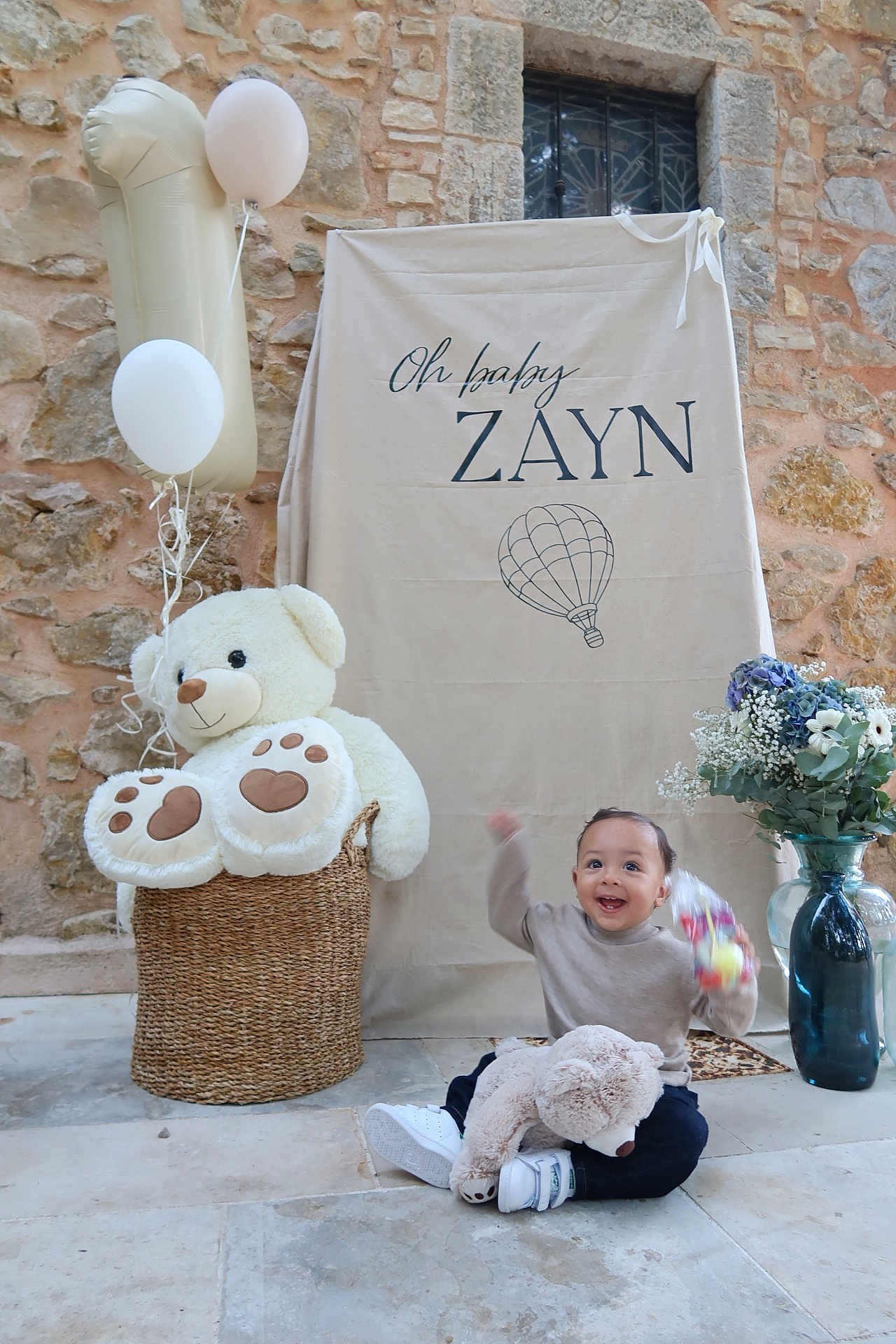 Zayn a rejoint le concours — aidez-le/la à gagner de superbes lots ! toddler, child, teddy_bear, balloons, basket, stone_wall, floor, toy, flowers, vase, backdrop, text, happy, smiling, indoor, decorations, clothing, sneakers, person, celebration