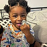 Marcus is registered to the contest to win money with this photo: toddler, child, pacifier, smiling, bed, pajamas, patterned_clothing, hair_puffs, indoor, happy, cute, person, young_child, black_hair, sitting, playful, face, closeup, infant, room