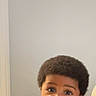 Marcus is registered to the contest to win money with this photo: baby, child, indoor, curly_hair, blue_shirt, portrait, face, skin, person, infant, young_child, afro, expression, seated, looking_at_camera, casual_clothing, home, cute, young, curious