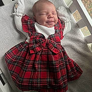 Amaya is registered to the contest to win money with this photo: baby, infant, crib, dress, red_plaid, mittens, smile, sleeping, cute, child, toddler, white, soft_lighting, bow, clothing, blanket, indoor, peaceful, portrait, newborn