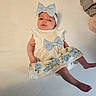 baby, infant, child, dress, blue_bow, headband, floral_pattern, lying_down, cute, adorable, clothing, fabric, person, skin, feet, arms, white_background, soft_lighting, portrait, newborn