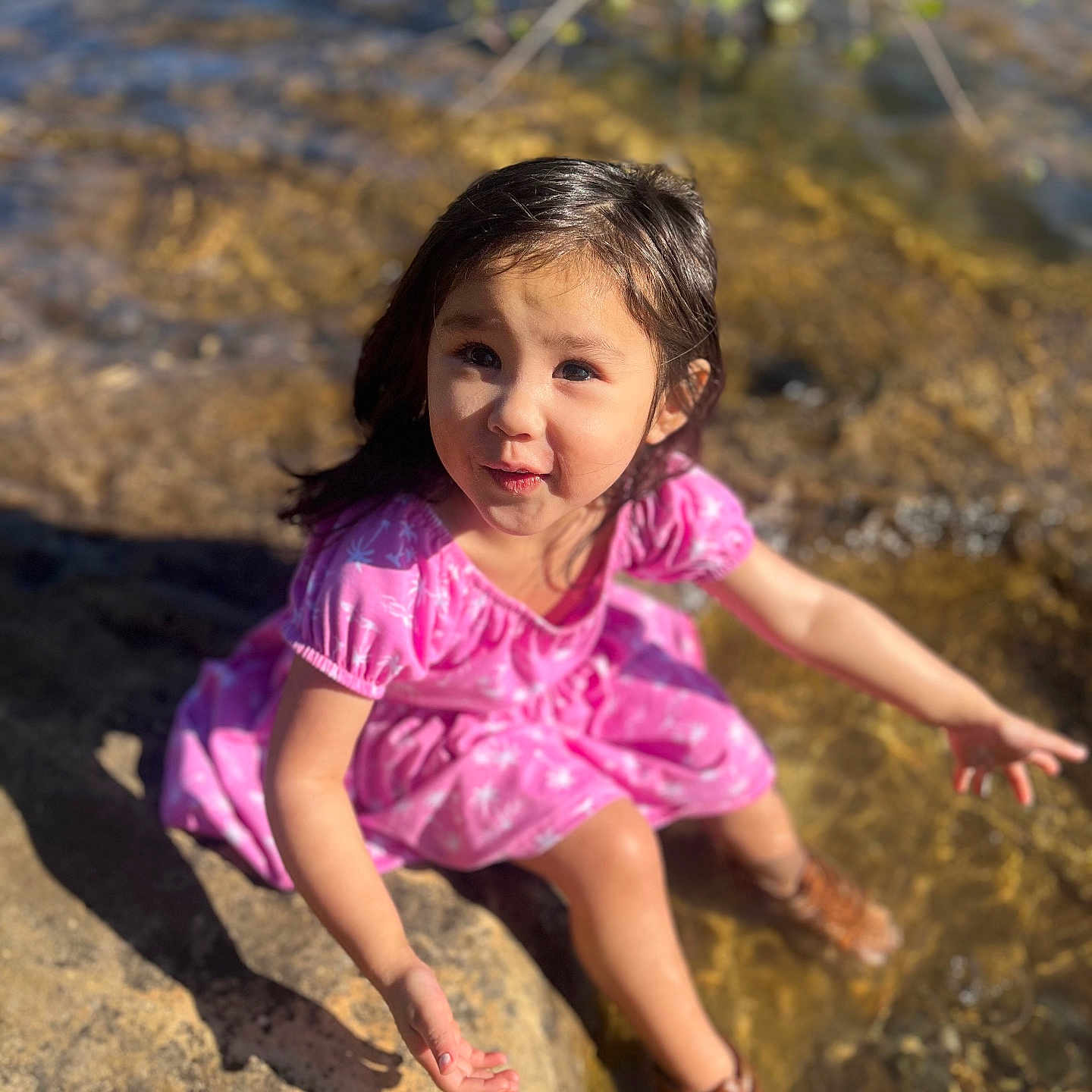 Zara is registered to the contest to win money with this photo: boots, child, curious, daylight, exploration, girl, happy, nature, outdoor, pink_dress, playful, portrait, rocks, shadow, sitting, summer, sunlight, water, water_edge, young
