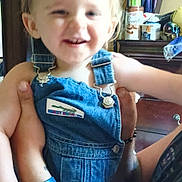 Alastor is registered to the contest to win money with this photo: toddler, child, denim_overalls, smiling, adult_hand, tattoo, wristband, indoor, dresser, clothing, can, furniture, person, holding, happy, face, arm, room, casual, portrait