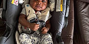 Michael is registered to the contest to win money with this photo: baby, infant, car_seat, seat_harness, clothing, black_shoes, patterned_pants, face, person, indoor, cushion, leather_couch, wood_floor, child, young_child, sitting, serious_expression, baby_boy, baby_girl, child_seat