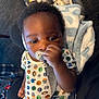 baby, black_hair, blanket, child, close_up, clothing, comfort, cute, face, hand, holding, indoor, infant, onesie, pacifier, patterned_clothing, person, seated, soft_texture, toddler