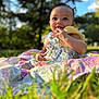 Truee is registered to the contest to win money with this photo: baby, child, outdoor, grass, quilt, colorful, smiling, happy, cute, portrait, nature, sunlight, dress, playful, infant, person, sitting, daytime, curly_hair, bright