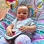 baby, smiling, infant, baby_seat, toy, rainbow, patterned_clothing, sitting, straps, cute, outdoor, playful, colorful, happy, child, soft_toy, curly_hair, face, bright, comfort