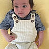 baby, infant, child, yellow_background, overalls, corduroy, checkered_shirt, wooden_buttons, lying_down, curious_expression, soft_texture, indoors, portrait, young_child, cute, small_hands, short_hair, casual_clothing, comfortable, resting