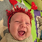 Walter is registered to the contest to win money with this photo: baby, infant, headband, red, heart, antennae, laughing, smiling, face, expression, play_mat, pattern, star, green, purple, beige, clothing, closeup, indoors, child