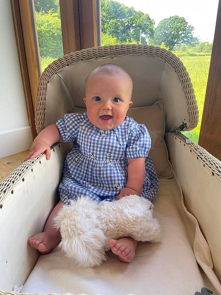Mabel is registered to the contest to win money with this photo: baby, baby_toddler_clothing, child, comfort, couch, eye, facial_expression, flooring, fun, hairstyle, lap, leisure, living_room, person, plant, skin, smile, thigh, toddler, tree